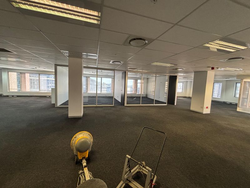 Spacious open-plan office area featuring glass-partitioned meeting rooms, suspended ceilings with integrated lighting, and carpeted flooring throughout.