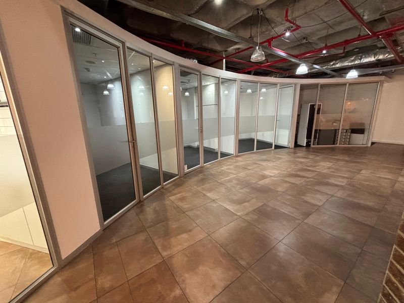 Modern office space featuring curved glass partition walls, tiled flooring, and an exposed industrial ceiling with integrated sprinkler systems.
