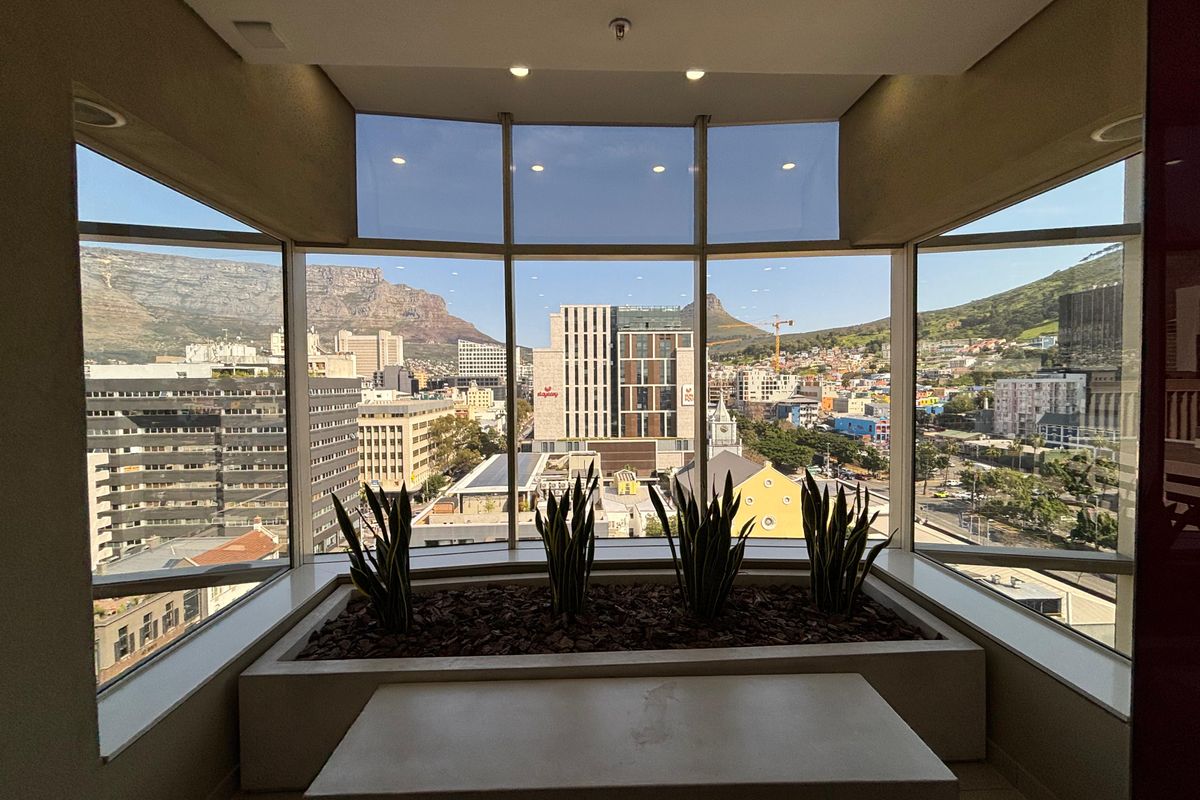A bright office space featuring expansive floor-to-ceiling windows with panoramic city and mountain views, complemented by a built-in planter box.