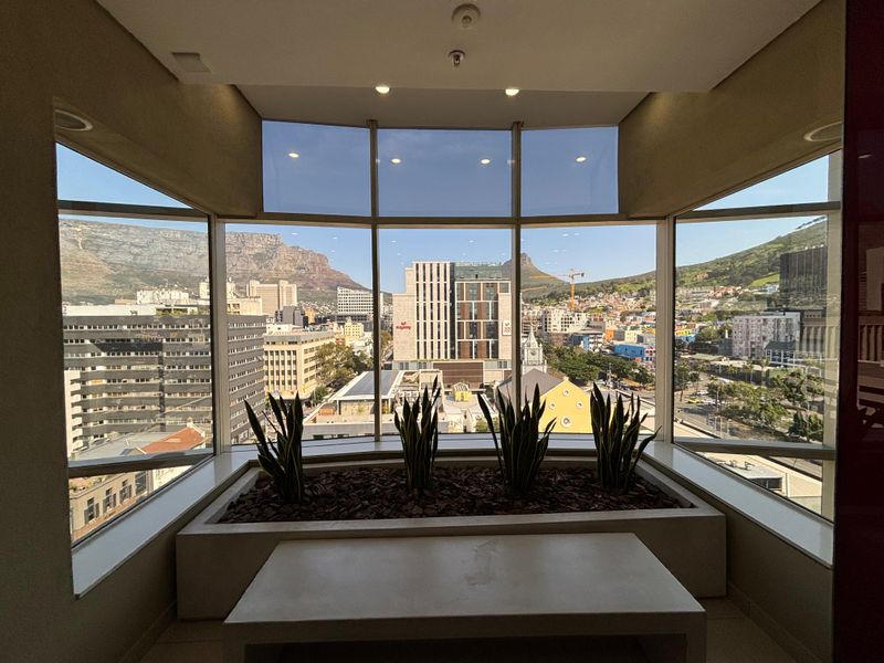 A bright office space featuring expansive floor-to-ceiling windows with panoramic city and mountain views, complemented by a built-in planter box.