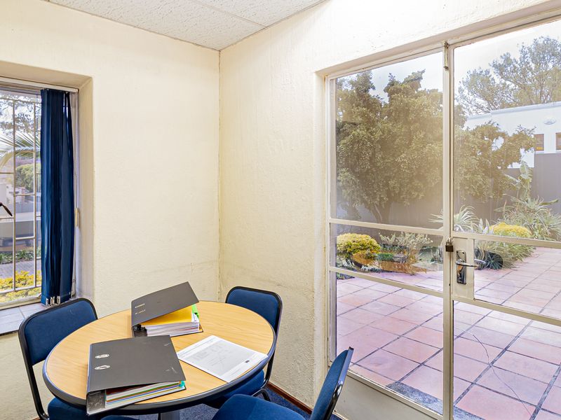 A functional office space featuring a sliding glass door with direct access to a tiled patio area and large windows providing natural light.
