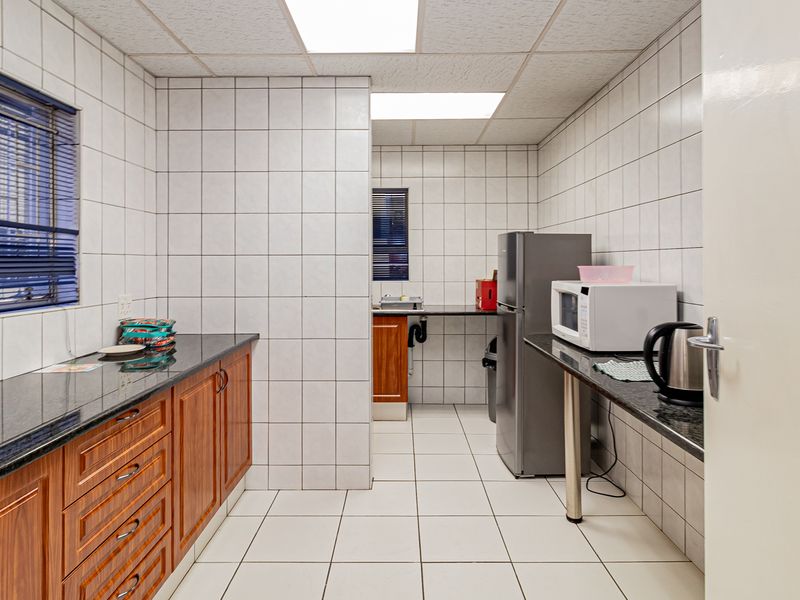 A functional office kitchen area featuring granite countertops, wooden cabinetry, and fully tiled walls and floors, providing a clean and practical workspace.