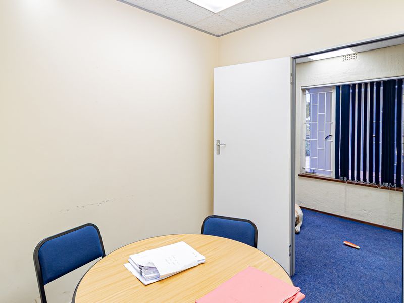 A functional office space featuring carpeted flooring, drop ceiling with integrated lighting, and security bars on the windows.
