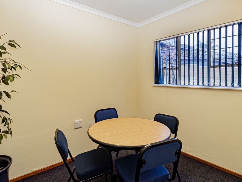 A functional office space featuring carpeted flooring, a window with vertical blinds, and neutral wall finishes.