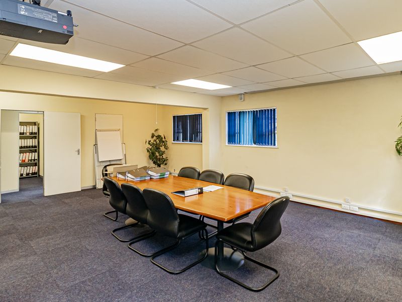 A functional office meeting room featuring a suspended ceiling, recessed lighting, carpeted flooring, and vertical window blinds.
