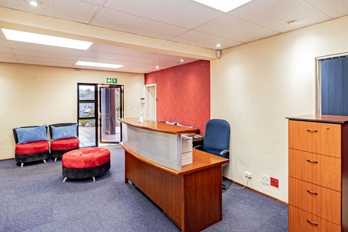 A functional office reception area featuring a built-in reception desk, suspended ceiling with recessed lighting, and direct access to an outdoor area.
