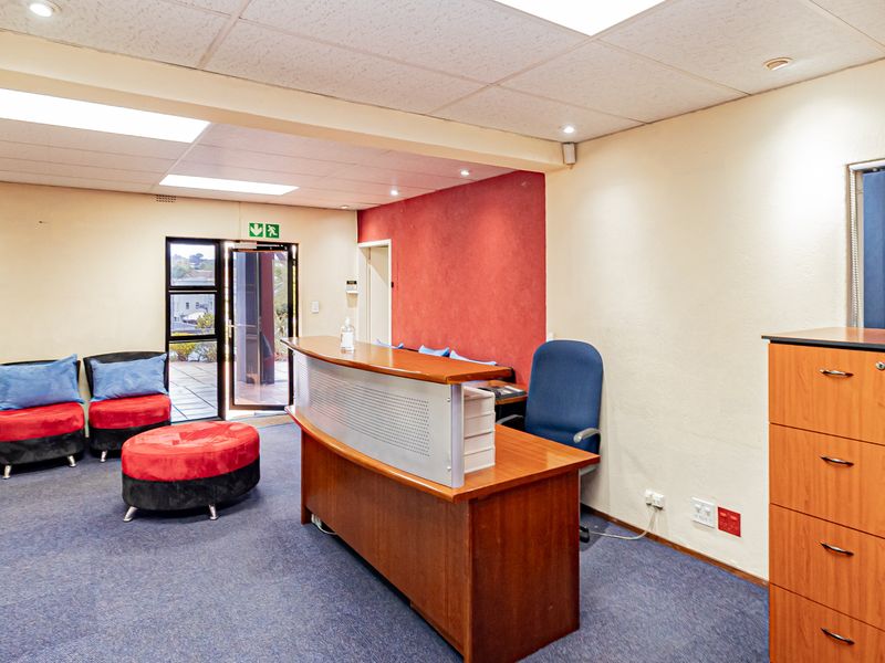 A functional office reception area featuring a built-in reception desk, suspended ceiling with recessed lighting, and direct access to an outdoor area.