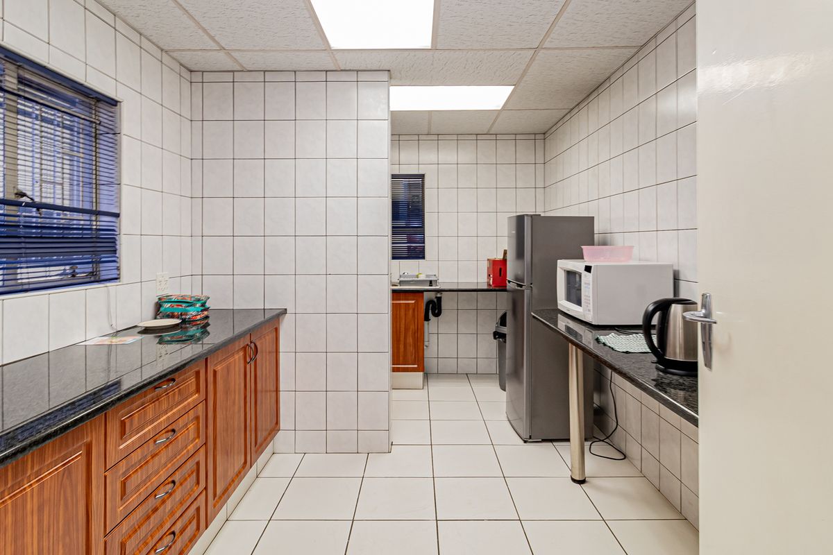 A functional office kitchen area featuring granite countertops, wooden cabinetry, and fully tiled walls and floors, providing a clean and practical workspace.