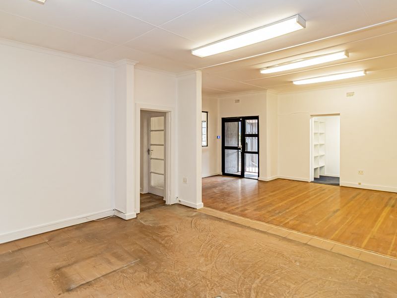 Spacious open-plan office area featuring hardwood flooring, bright fluorescent lighting, and built-in shelving, offering a versatile workspace layout.