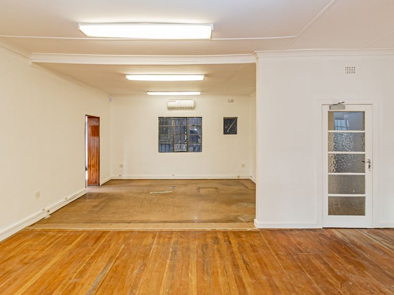 An empty, open-plan office space featuring timber flooring, fluorescent lighting, and an integrated air conditioning unit.