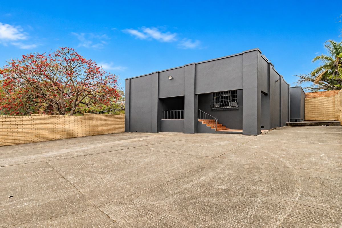 Rear exterior view of the office building featuring a large concrete parking area, brick boundary walls, and secure access points.