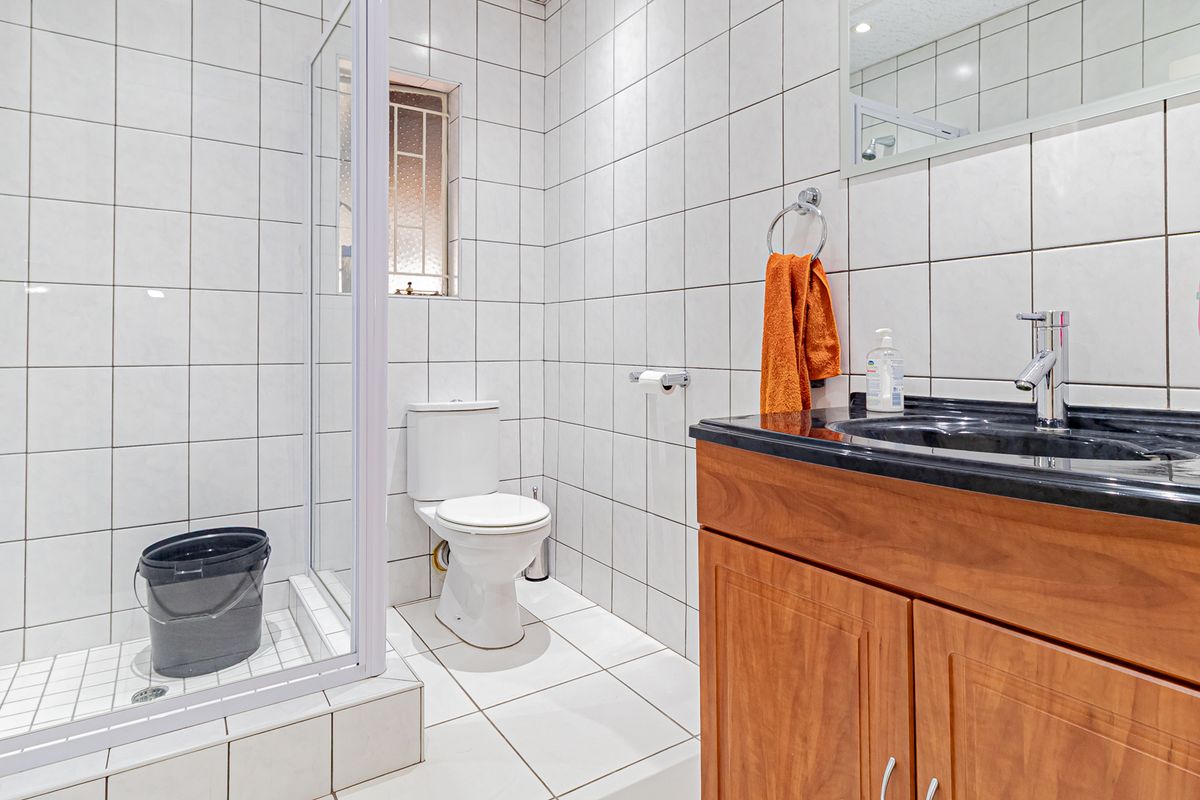 A functional bathroom featuring a shower enclosure, toilet, and a vanity cabinet with a basin, finished with white wall and floor tiles.