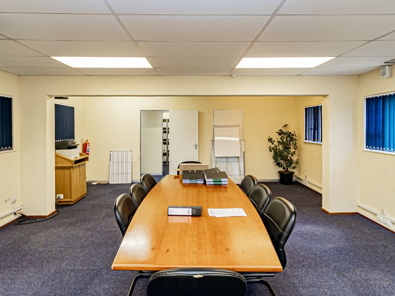 A functional office meeting room featuring carpeted flooring, suspended ceiling tiles, recessed lighting, and vertical window blinds.