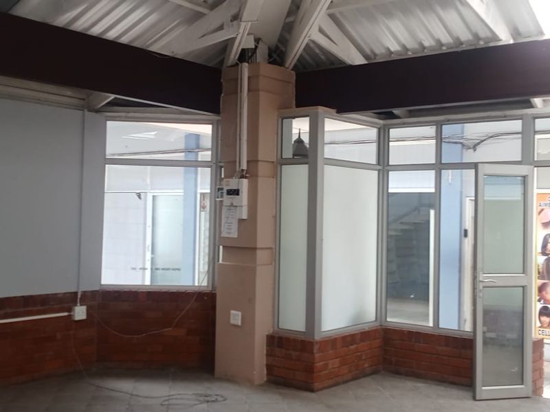 Open-plan retail space featuring exposed roof trusses, brick base wall detailing, and extensive aluminium-framed glass frontage for high visibility.