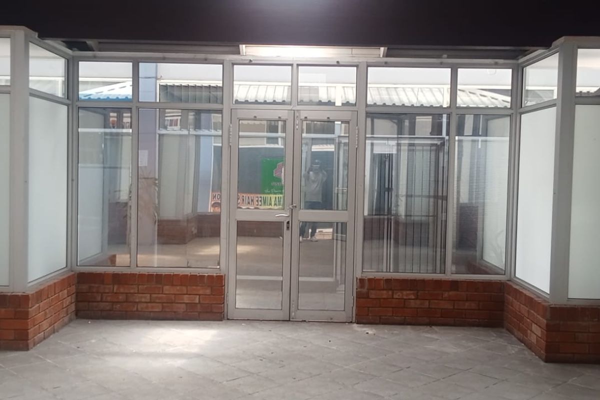 A retail storefront entrance featuring aluminium-framed glass doors and windows with a brick base, providing a clear view into the vacant commercial space.