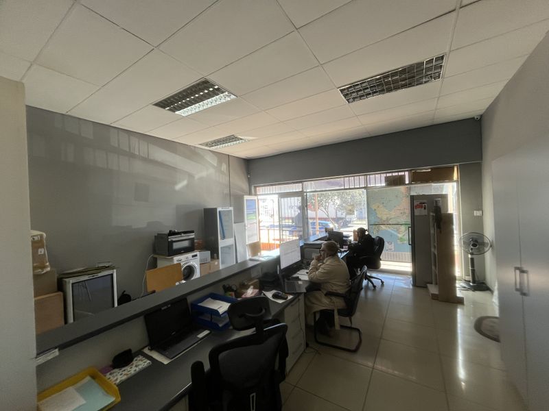 Functional office space featuring a built-in reception counter, tiled flooring, and a large glass storefront window providing natural light.