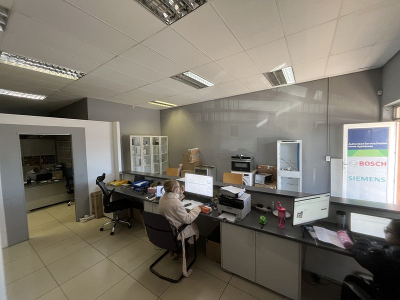 A functional office reception area featuring a long built-in service counter, tiled flooring, and a suspended ceiling with integrated lighting.