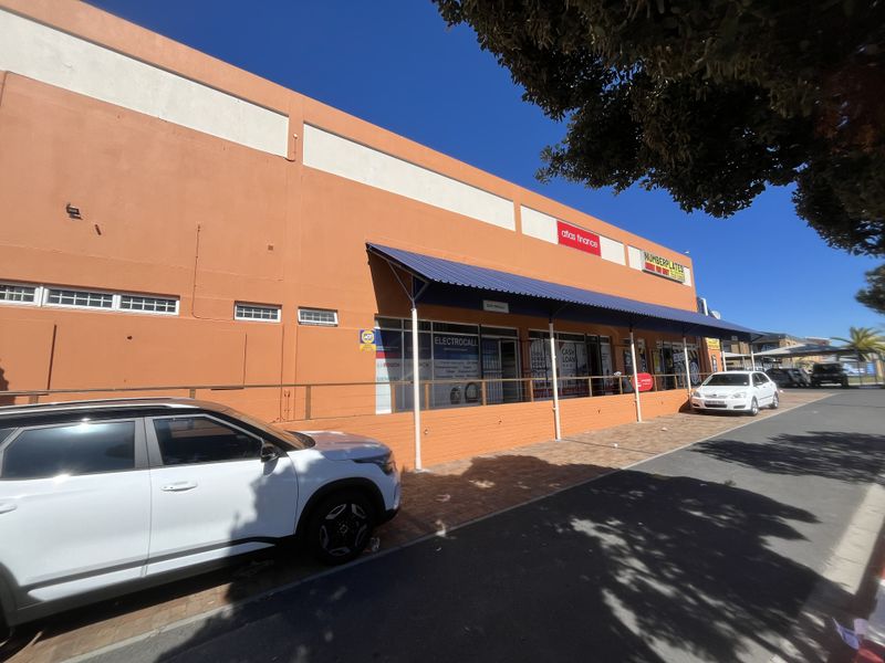 Front exterior view of a commercial building featuring a paved walkway, metal awning, and multiple storefront entrances.