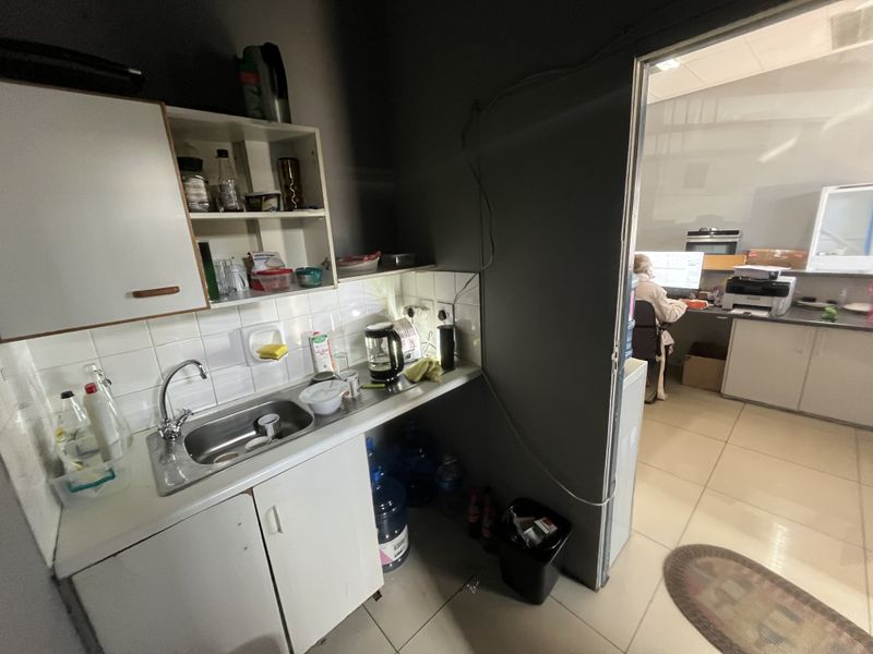 A compact scullery or kitchenette area featuring a stainless steel sink, tiled splashback, and built-in cabinetry, adjacent to an office workspace.