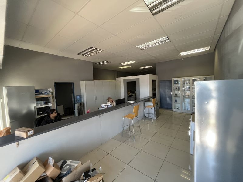 A functional office space featuring a built-in reception counter, tiled flooring, suspended ceiling with recessed lighting, and integrated storage cabinetry.