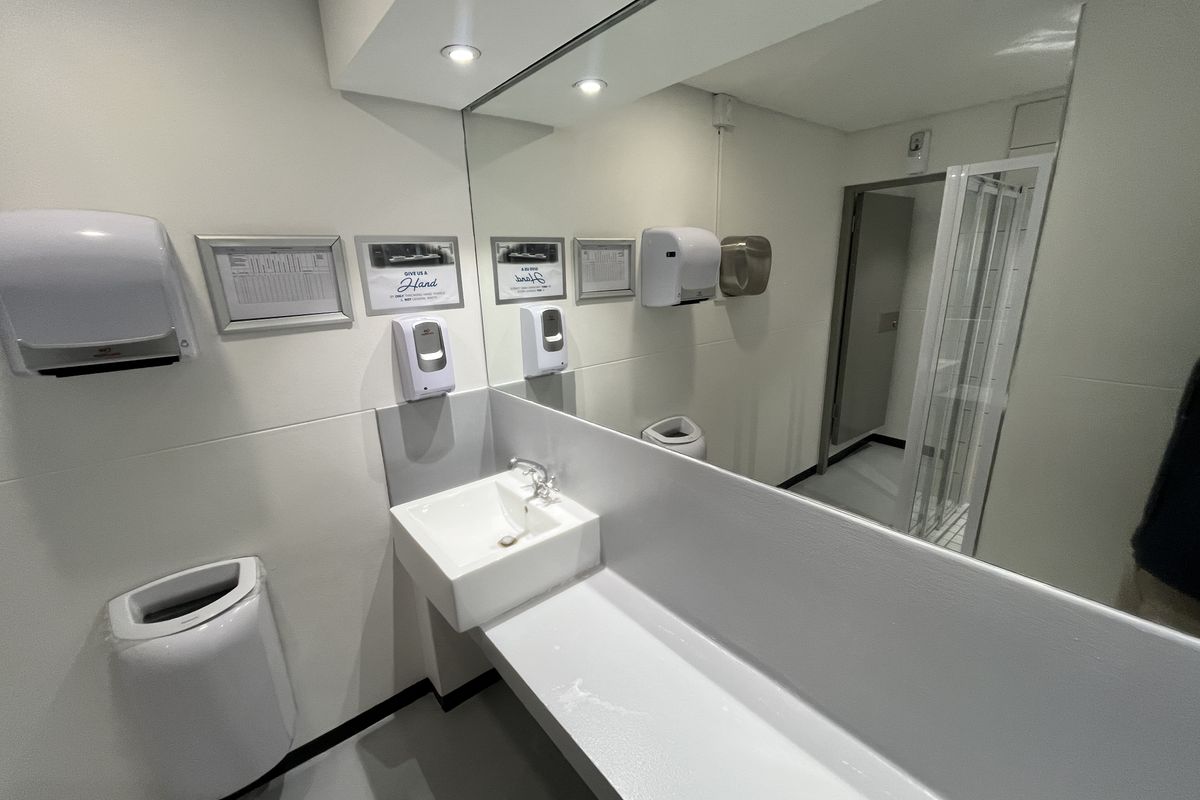 Modern office bathroom featuring a wall-mounted basin, large vanity mirror, recessed lighting, and a separate shower enclosure with clean, functional finishes.