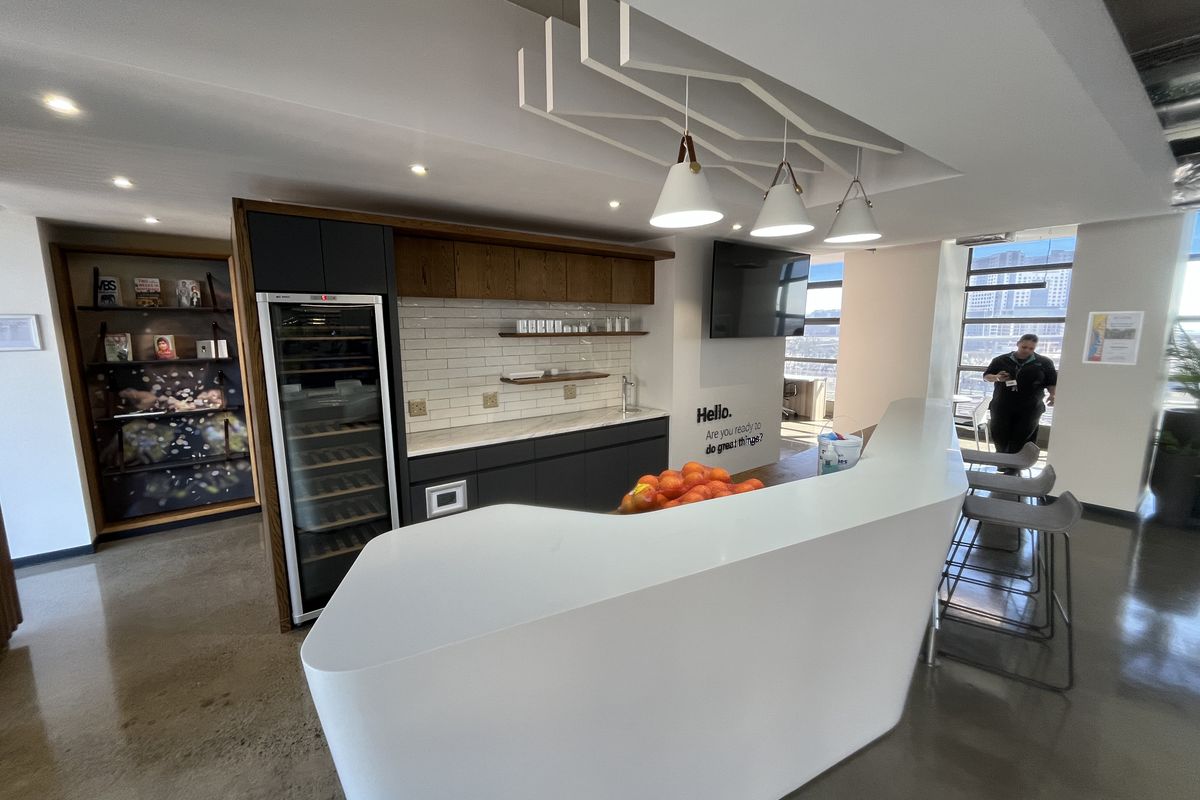 Modern office kitchen area featuring a sleek curved breakfast bar, integrated wine cooler, subway tile backsplash, and polished concrete floors with contemporary pendant lighting.