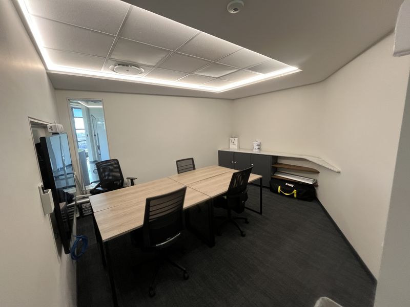 A modern office space featuring recessed ceiling lighting, suspended ceiling tiles, built-in cabinetry, and carpeted flooring, providing a professional work environment.