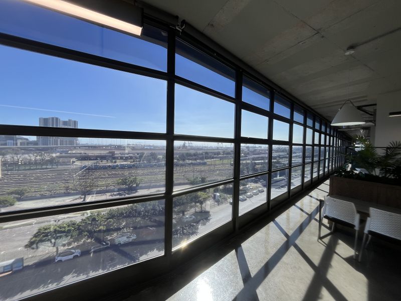 Modern office space featuring expansive floor-to-ceiling steel-framed windows, exposed concrete ceilings, and polished concrete floors with an urban industrial aesthetic.
