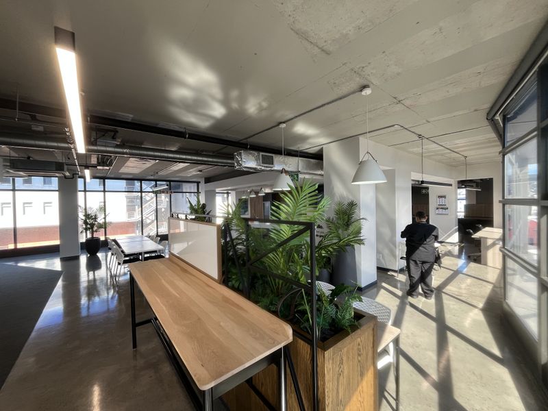 Modern open-plan office space featuring polished concrete floors, exposed industrial ceilings with ducting, and large windows providing ample natural light.