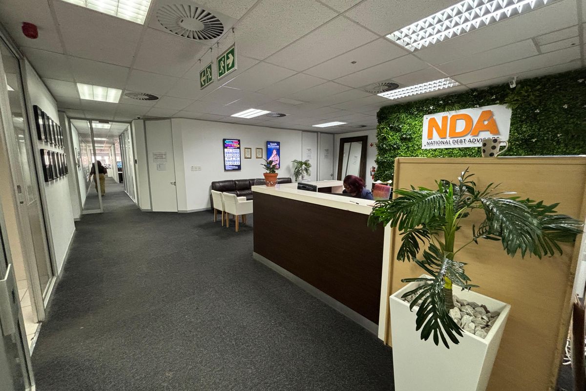 Professional office reception area featuring a built-in reception desk, suspended ceiling with recessed lighting, and glass-partitioned hallway access.