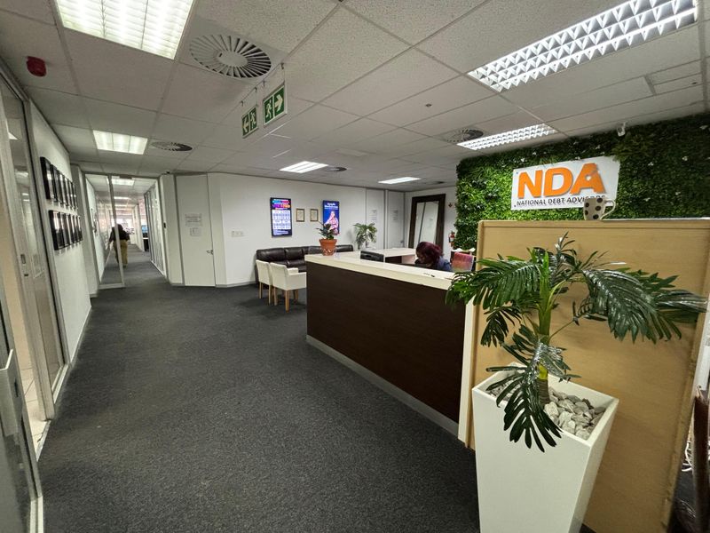 Professional office reception area featuring a built-in reception desk, suspended ceiling with recessed lighting, and glass-partitioned hallway access.