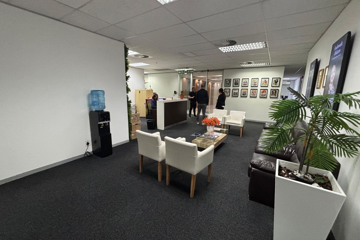 A professional office reception area featuring a built-in reception desk, suspended ceiling with recessed lighting, and dark carpet flooring.