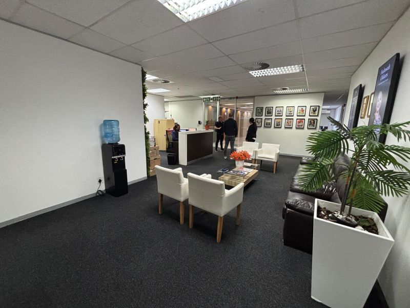 A professional office reception area featuring a built-in reception desk, suspended ceiling with recessed lighting, and dark carpet flooring.