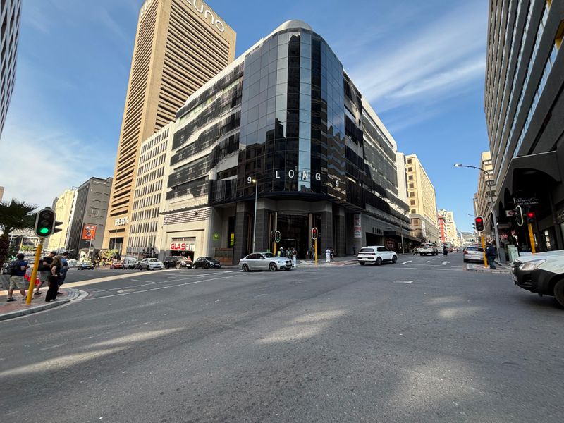 Street level view of a modern commercial office building with a prominent glass facade located on a busy city corner.