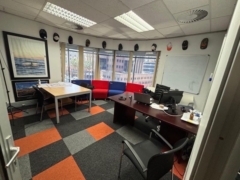 A functional office space featuring carpet tiles, suspended ceilings with recessed lighting, and large windows providing natural light and urban views.