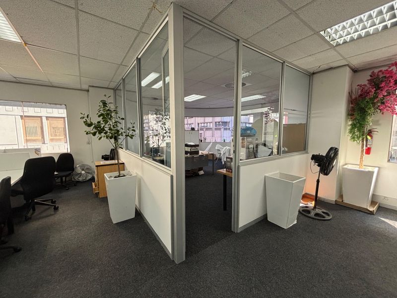 A professional office space featuring glass partition walls, suspended ceilings, and carpeted flooring, providing a functional layout for a modern workspace.