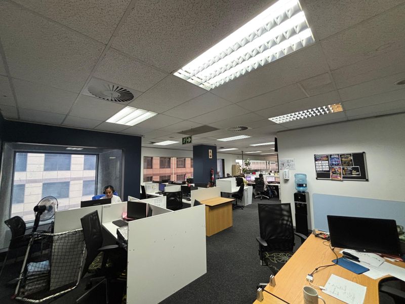 Open-plan office space featuring suspended ceilings, recessed lighting, air conditioning vents, and modular partition workstations with carpeted flooring.