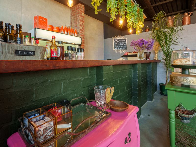 A rustic restaurant bar area featuring a painted brick service counter, exposed brick detailing, and exposed timber ceiling beams with industrial-style pendant lighting.