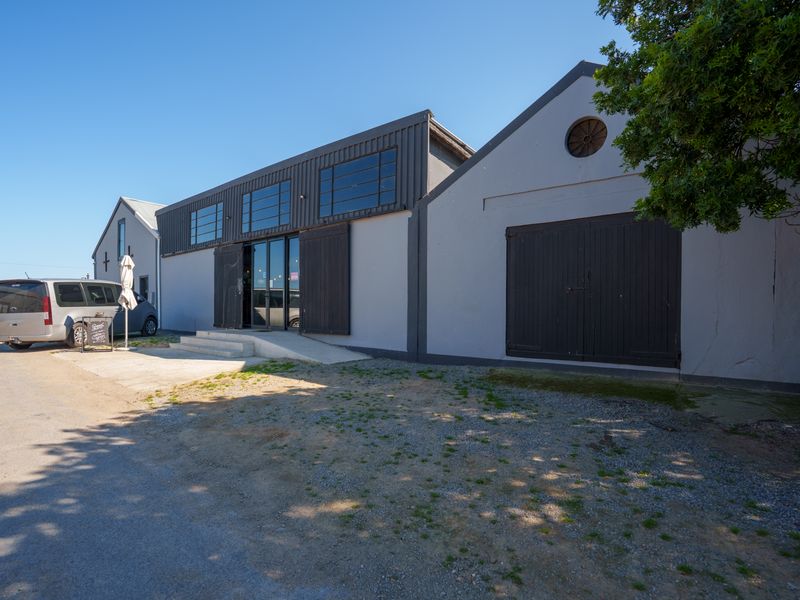 Front exterior view of an industrial-style restaurant building featuring metal cladding, large steel-framed windows, and sliding barn-style doors.