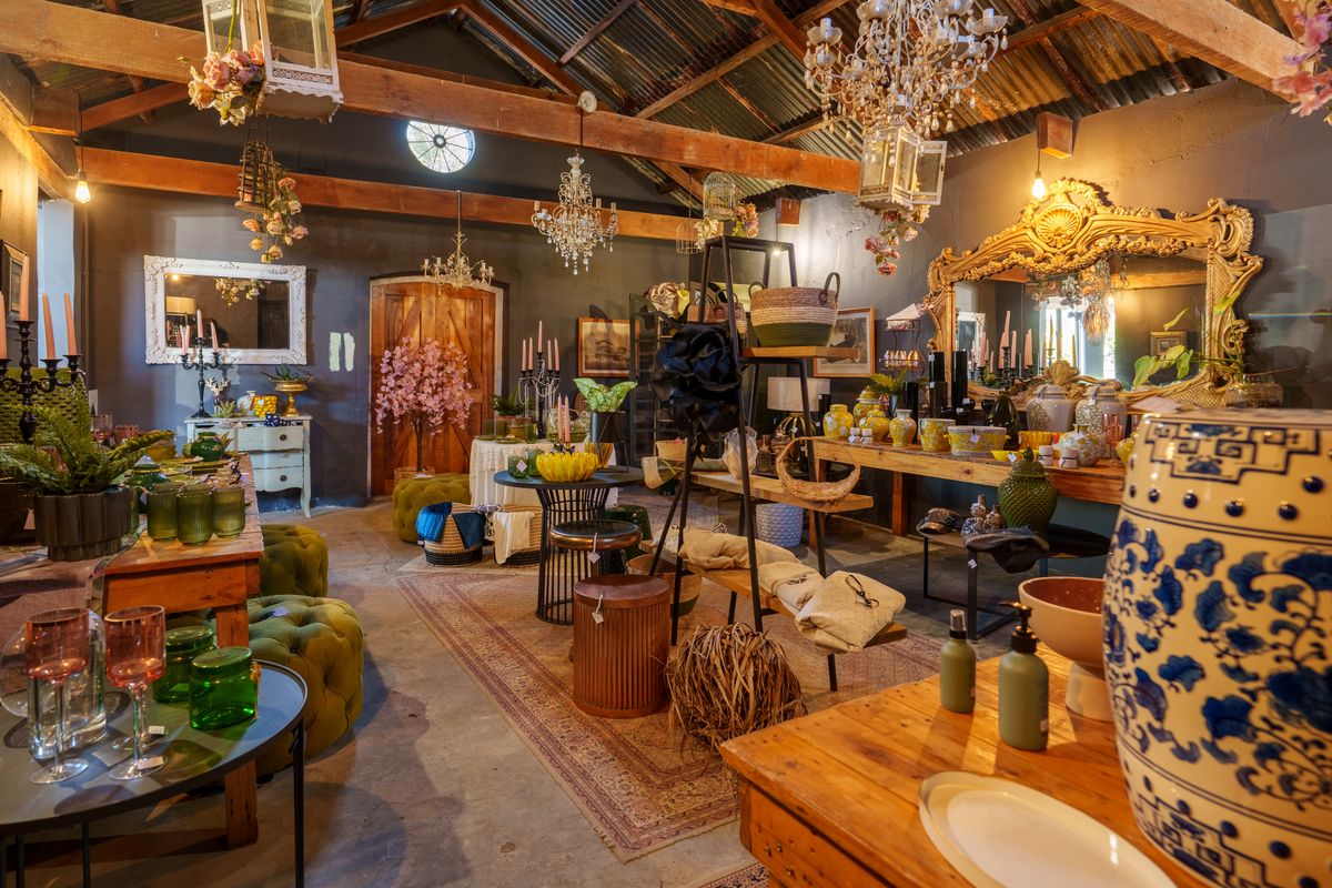A rustic interior space featuring exposed timber beams, a corrugated metal ceiling, and an arched wooden door, currently utilized as a retail display area.