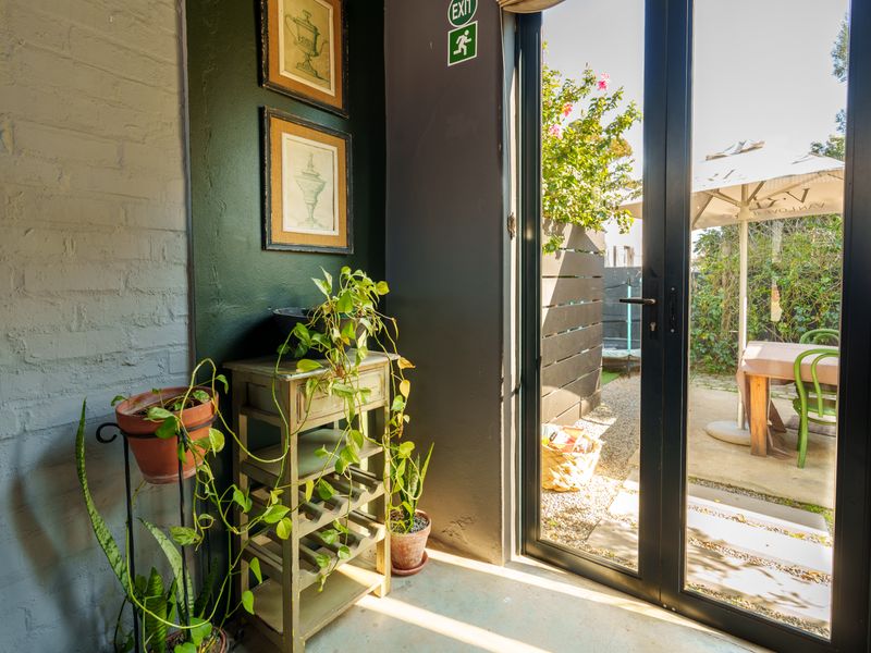 An interior entry area featuring dark painted walls, a textured brick accent wall, and double glass doors providing direct access to an outdoor patio.