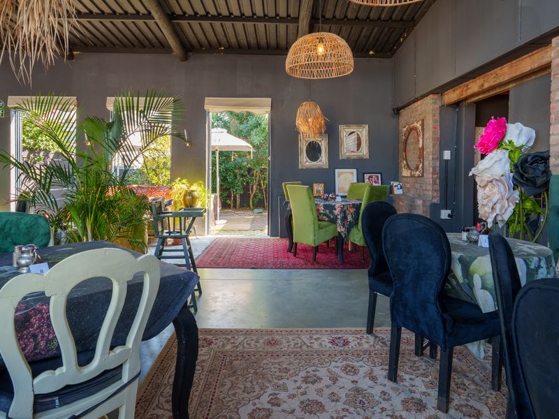 An open-plan restaurant dining area featuring exposed brick walls, a high exposed beam ceiling, and polished concrete floors with direct access to an outdoor space.