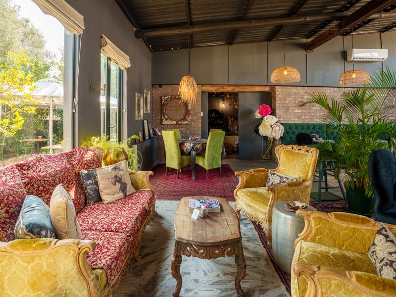 An open-plan restaurant dining area featuring exposed brick walls, high exposed beam ceilings, and large windows overlooking a garden space.