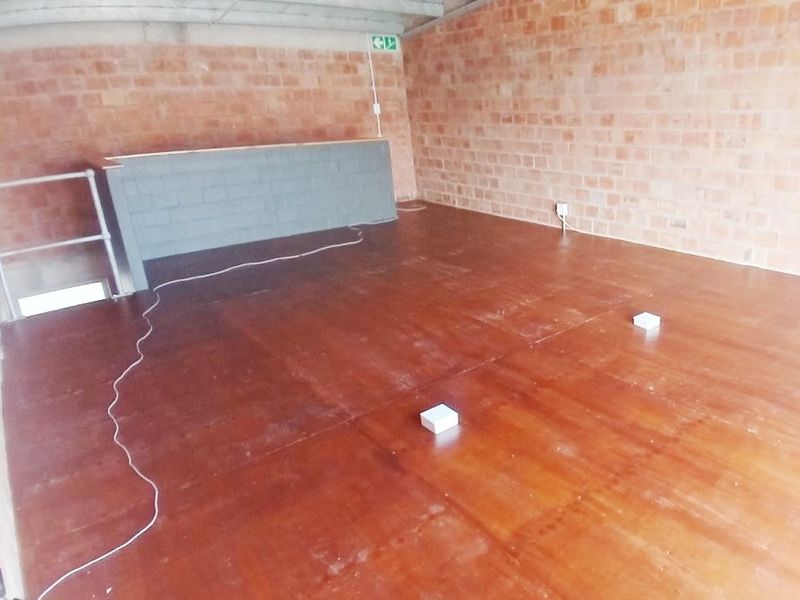 An empty office space featuring exposed brick walls, exposed ceiling beams, and basic utility finishes, suitable for custom fit-out.