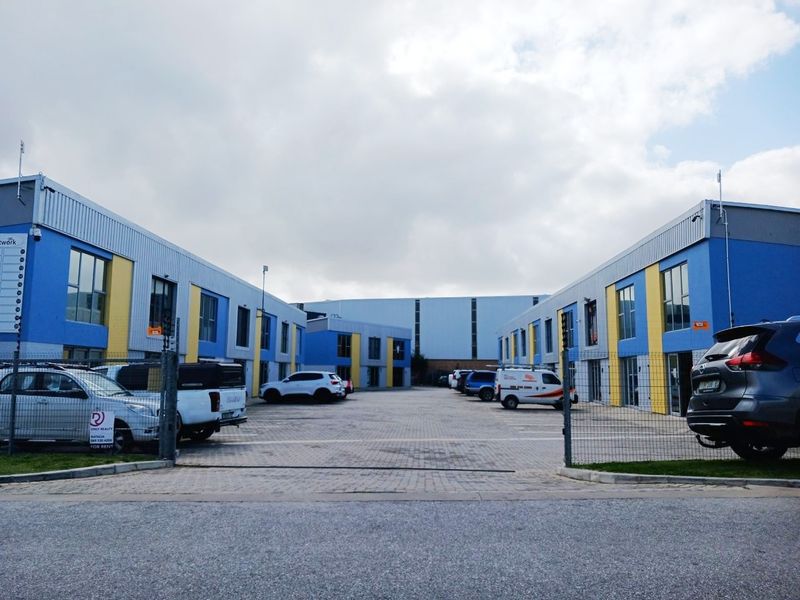 A view of a modern commercial office park featuring paved parking areas and blue and yellow metal-clad building facades.