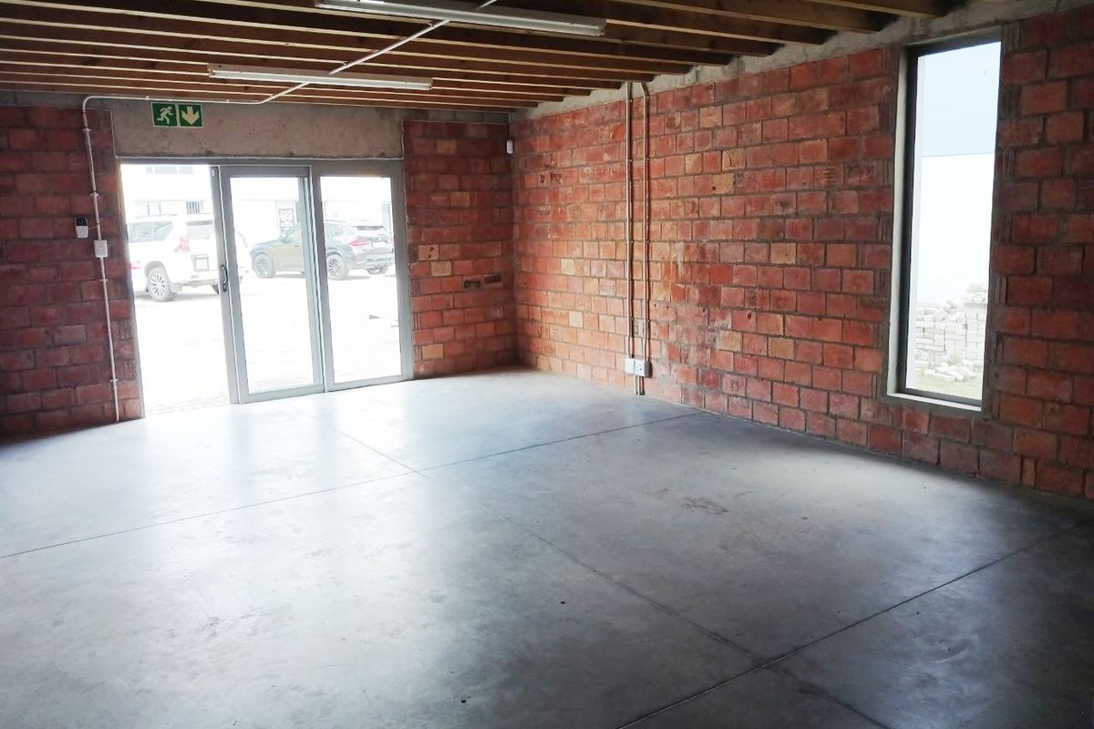 An industrial-style office space featuring exposed brick walls, concrete flooring, and exposed timber ceiling joists with natural light from a vertical window.