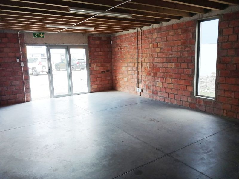 An industrial-style office space featuring exposed brick walls, concrete flooring, and exposed timber ceiling joists with natural light from a vertical window.