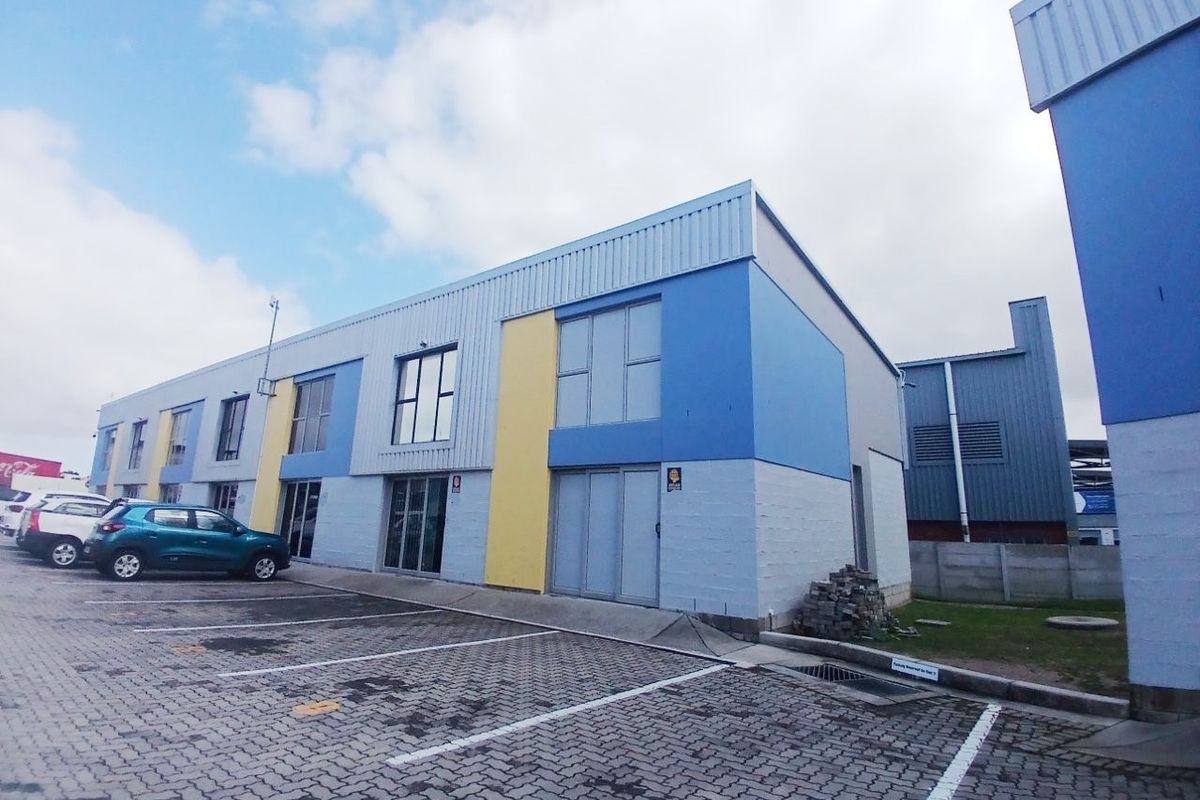 Exterior view of a modern commercial office building featuring metal cladding, paved parking bays, and aluminum window frames.