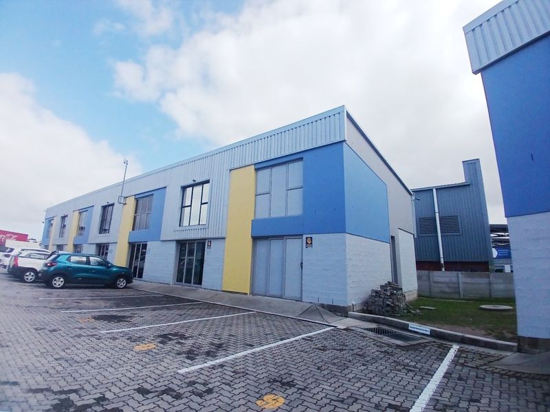 Exterior view of a modern commercial office building featuring metal cladding, paved parking bays, and aluminum window frames.