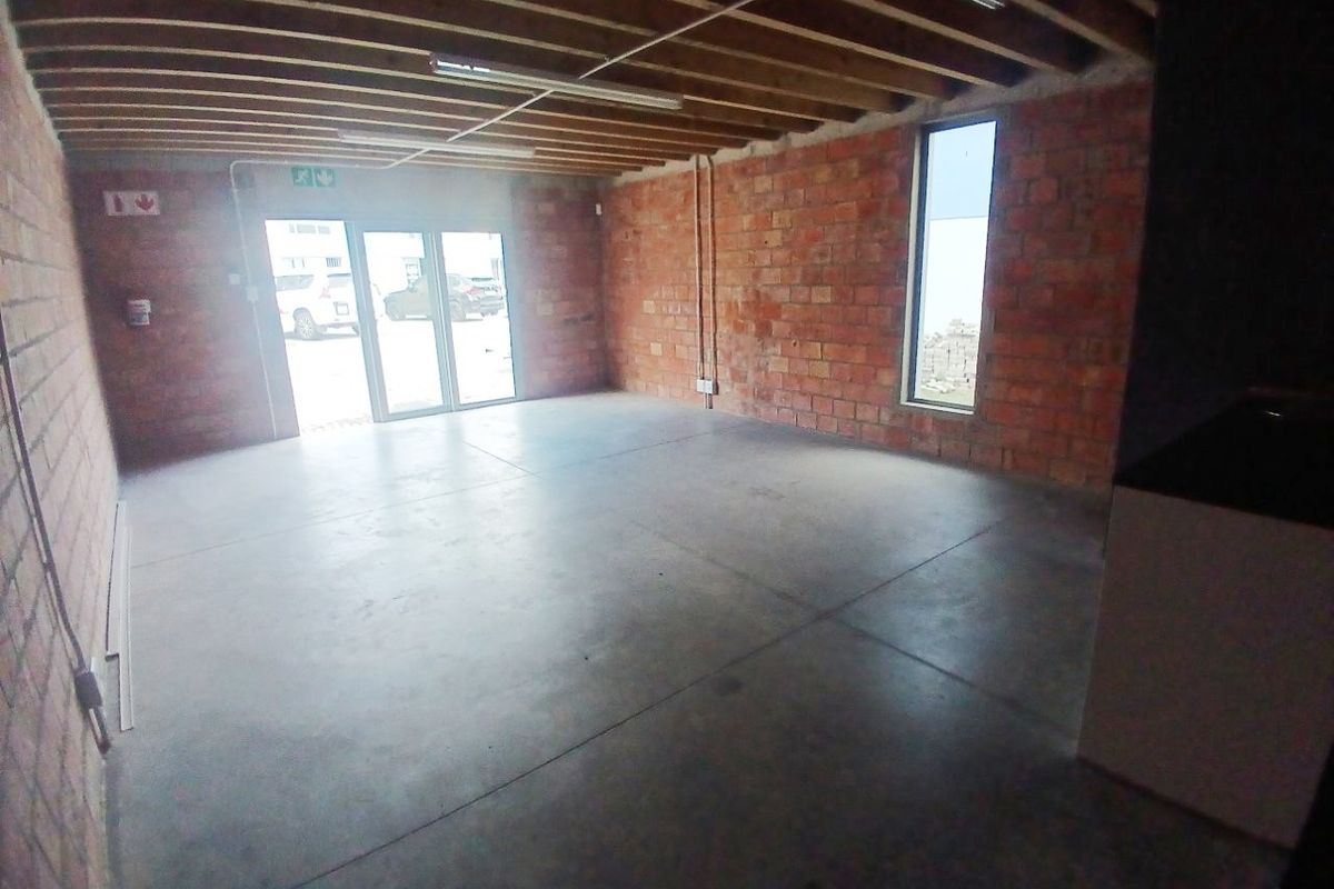 An open-plan office space featuring exposed brick walls, concrete flooring, and exposed timber ceiling joists, offering a modern industrial aesthetic.